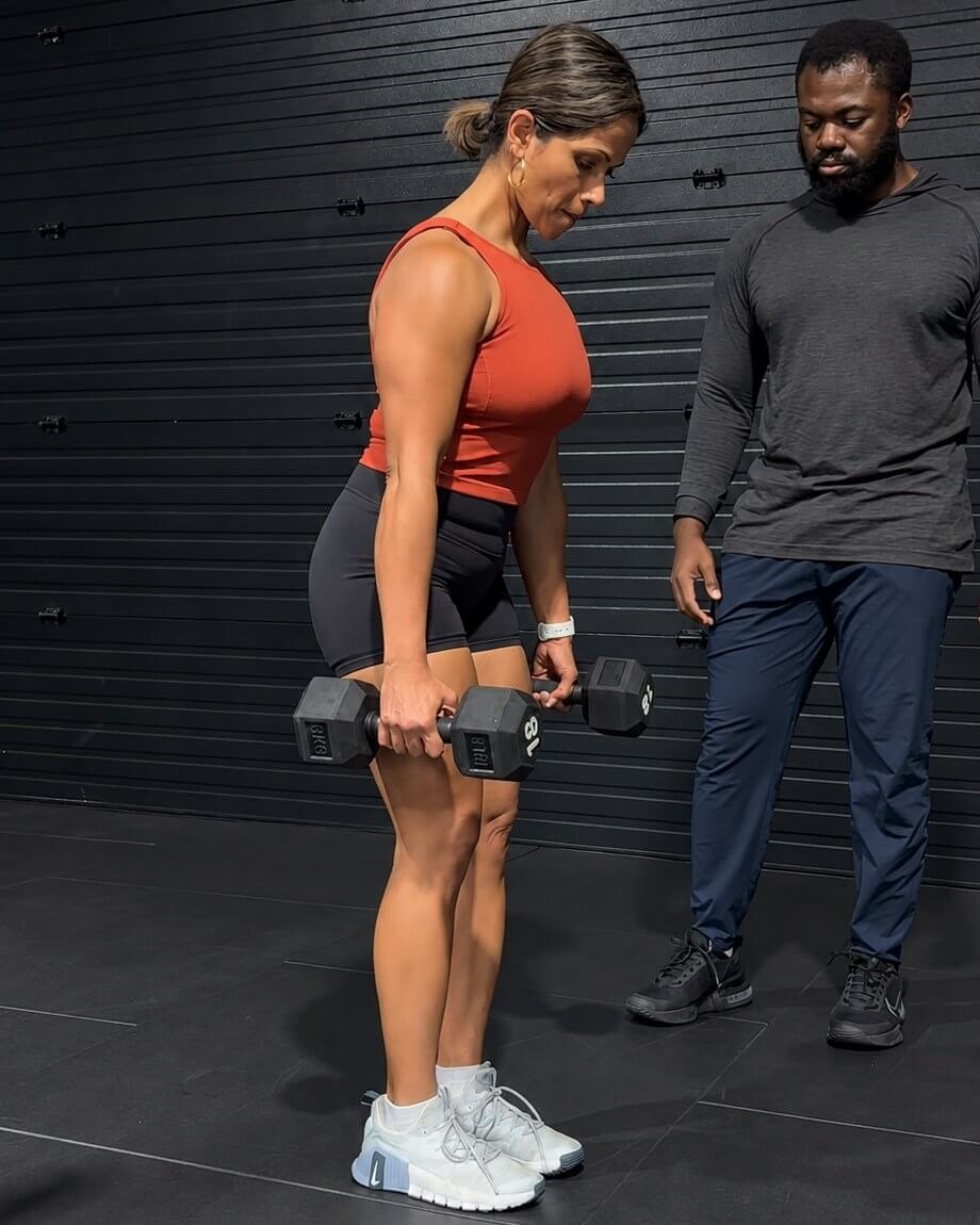 Doug Koomson, right, watches a client's form as she holds two dumbbells